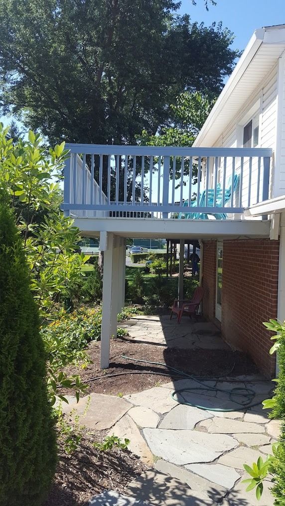 Back patio with white railing, brick house wall, stone path, and lush green garden.