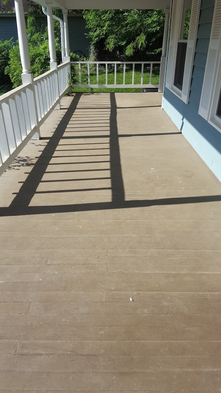 Sunlit wooden porch with white railings and blue house siding, casting long shadows overlooking green trees