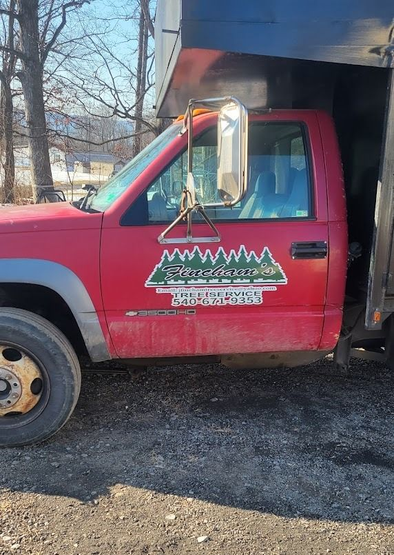 Red work truck parked on gravel, with a black dump bed and tree logo on the door.