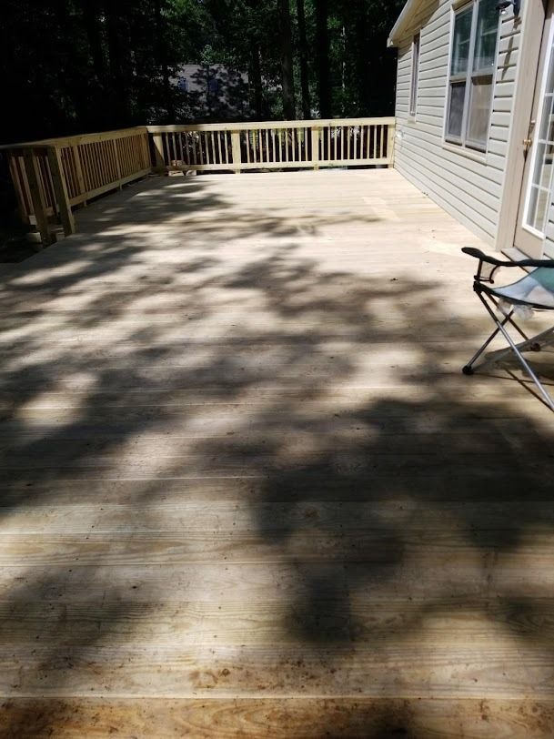 Wooden deck beside a house, with railing, dappled sunlight, and a folding chair on the right.
