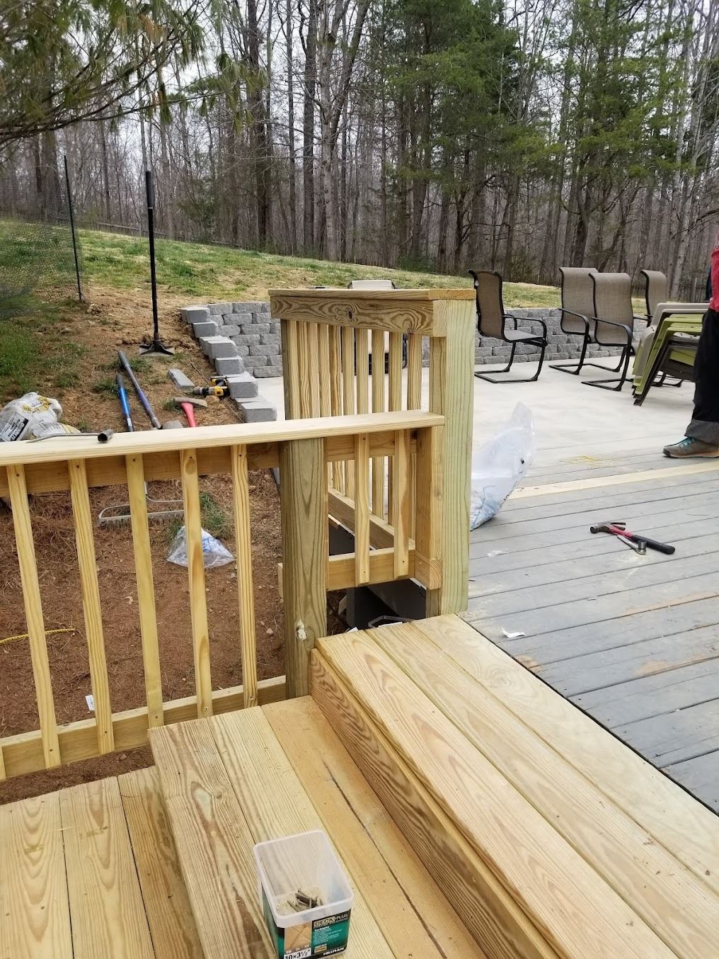 Wooden deck stairs and railing under construction overlooking a wooded backyard patio.