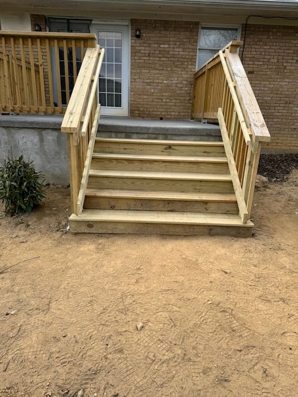 Wooden front steps with railings leading to a brick house entrance over dirt ground.