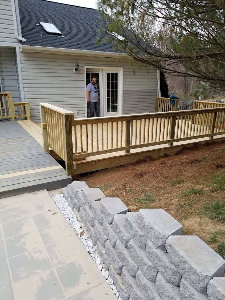 Wooden accessibility ramp beside a house deck, with a person standing near the doorway.