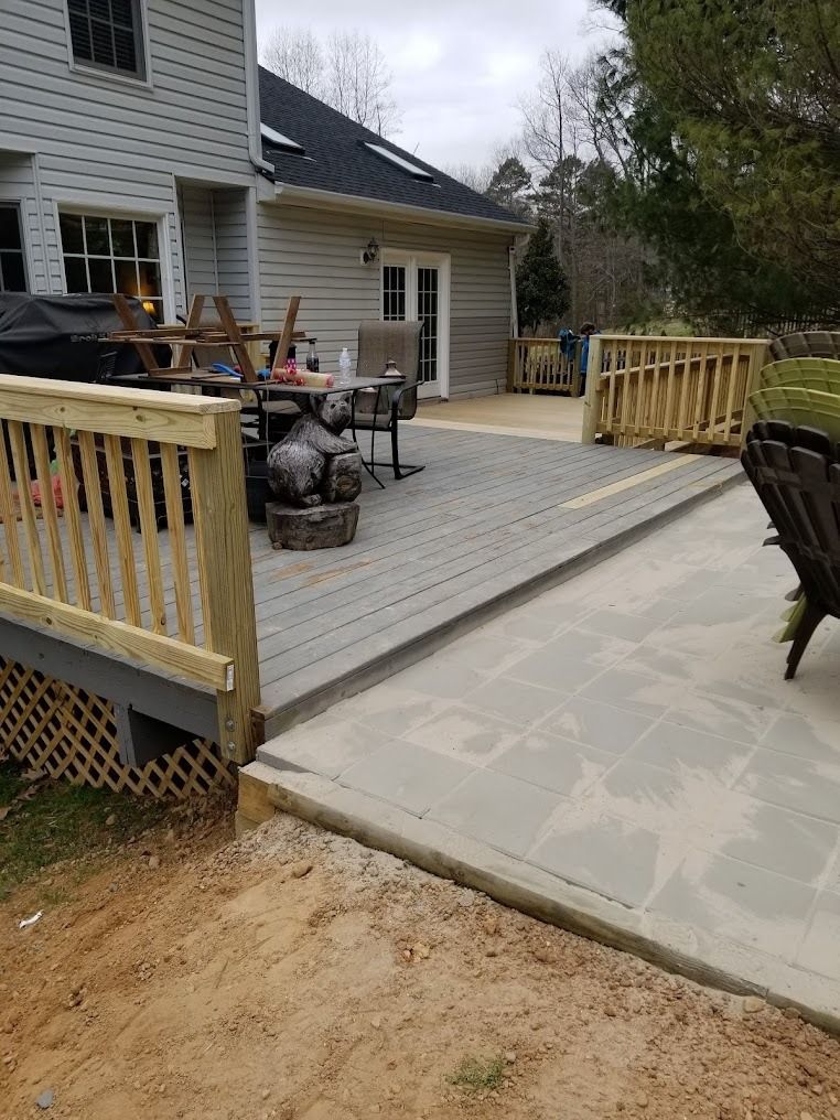 Backyard deck with railing and patio furniture beside a house, next to a concrete slab and dirt