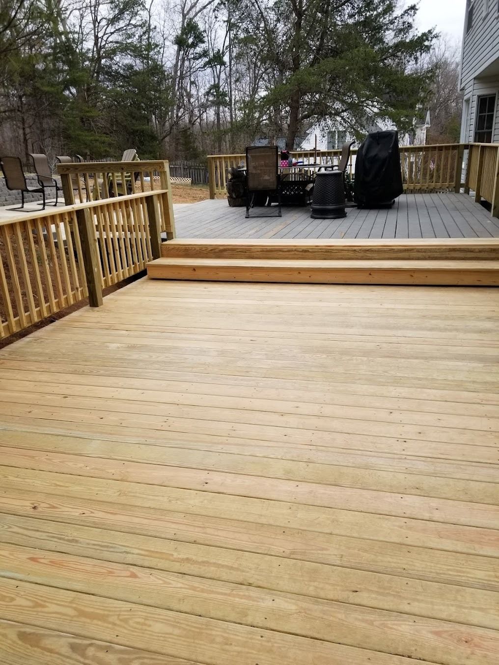 Wooden backyard deck with railings, steps, and patio furniture in a snowy yard