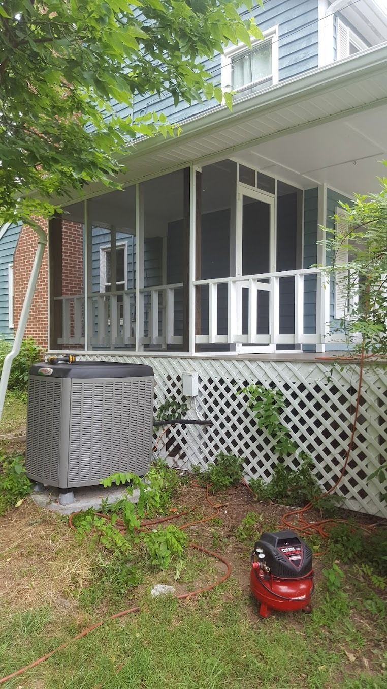 Porch with white railing, lattice skirting, and a red lawn mower in the grass beside a house.