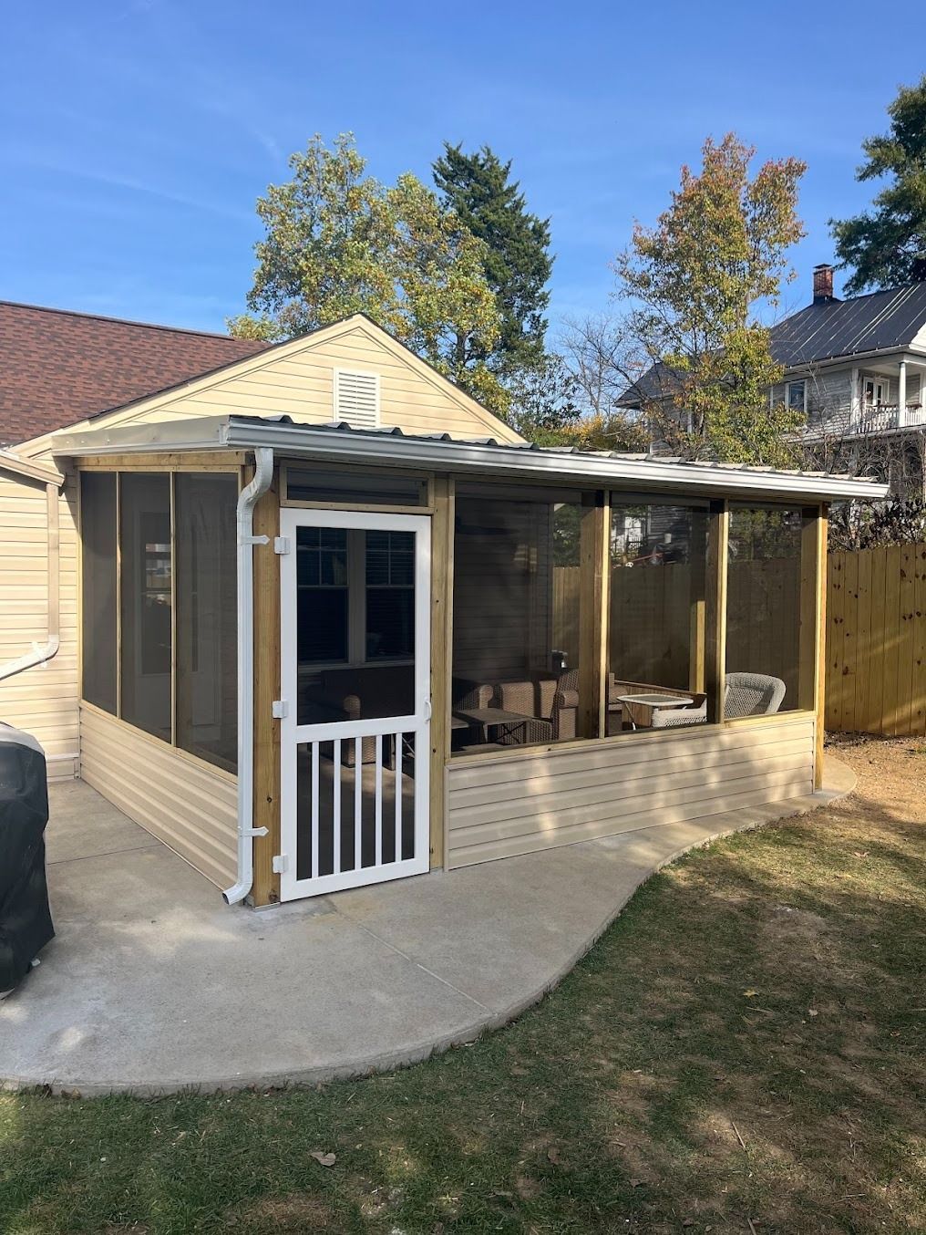Small beige screened porch attached to a house, with white trim and a sloped roof.