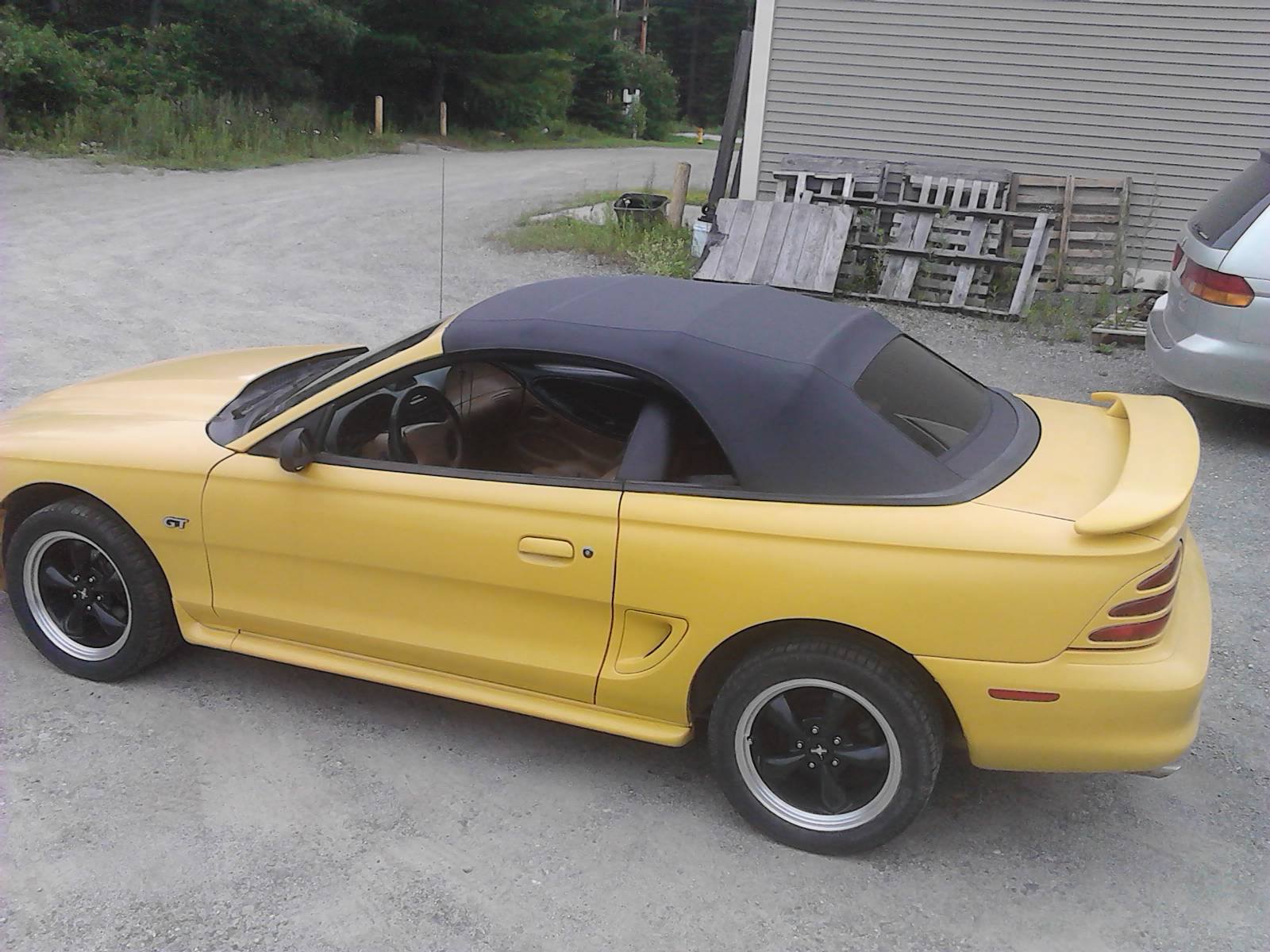 A yellow convertible mustang is parked in a parking lot