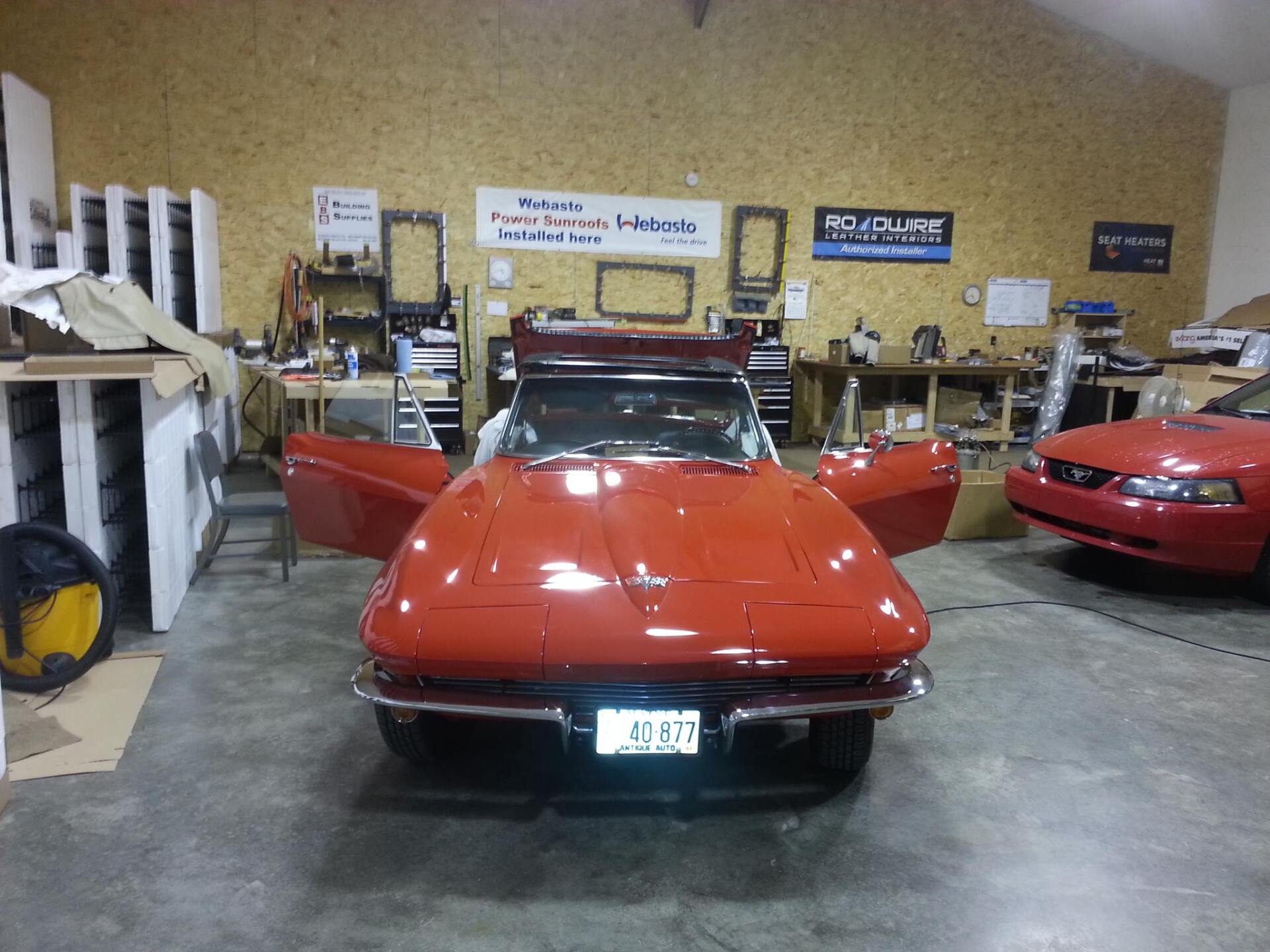A red corvette is parked in a garage with its doors open