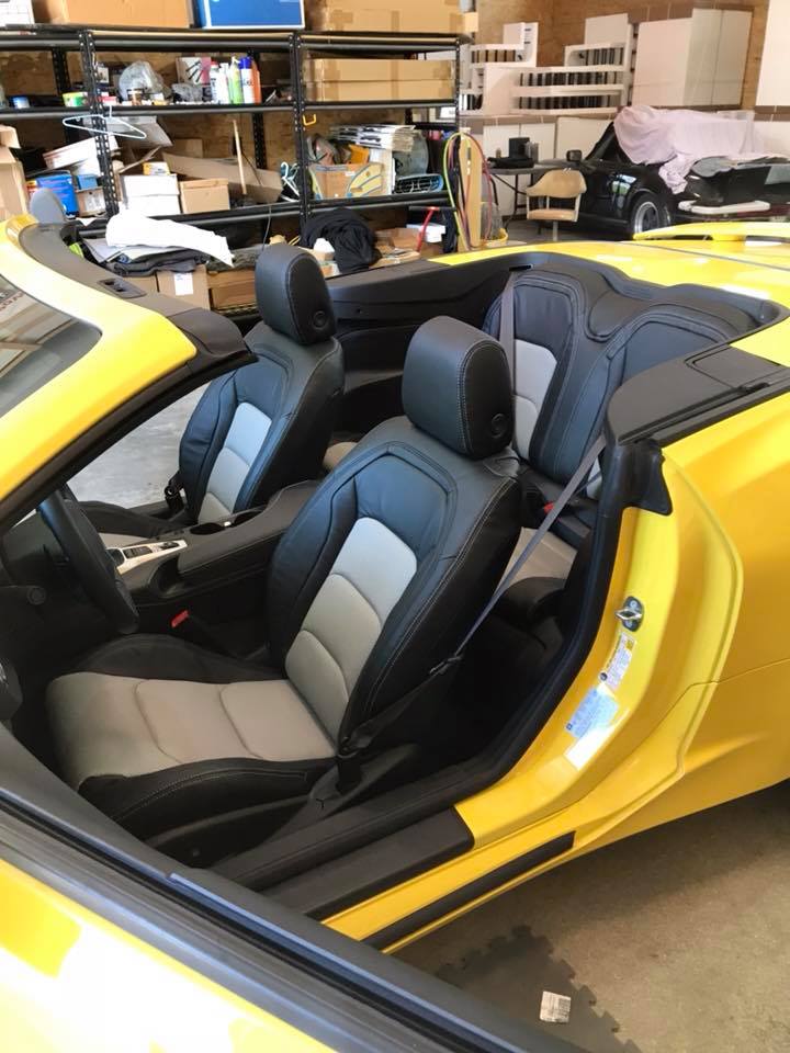 A yellow convertible car with black and gray seats is parked in a garage.