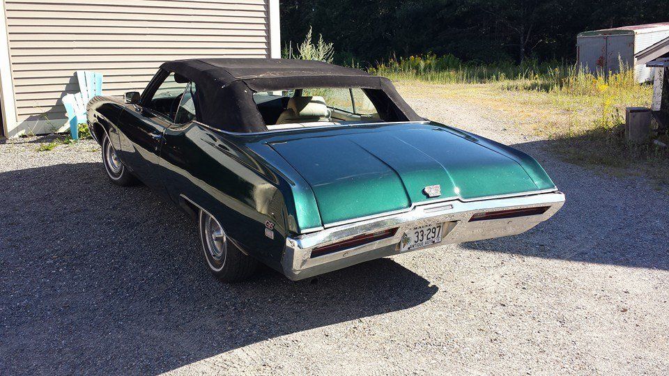 A green car with a black top is parked in a driveway.