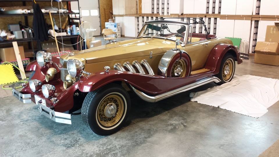 A red and gold vintage car is parked in a garage.