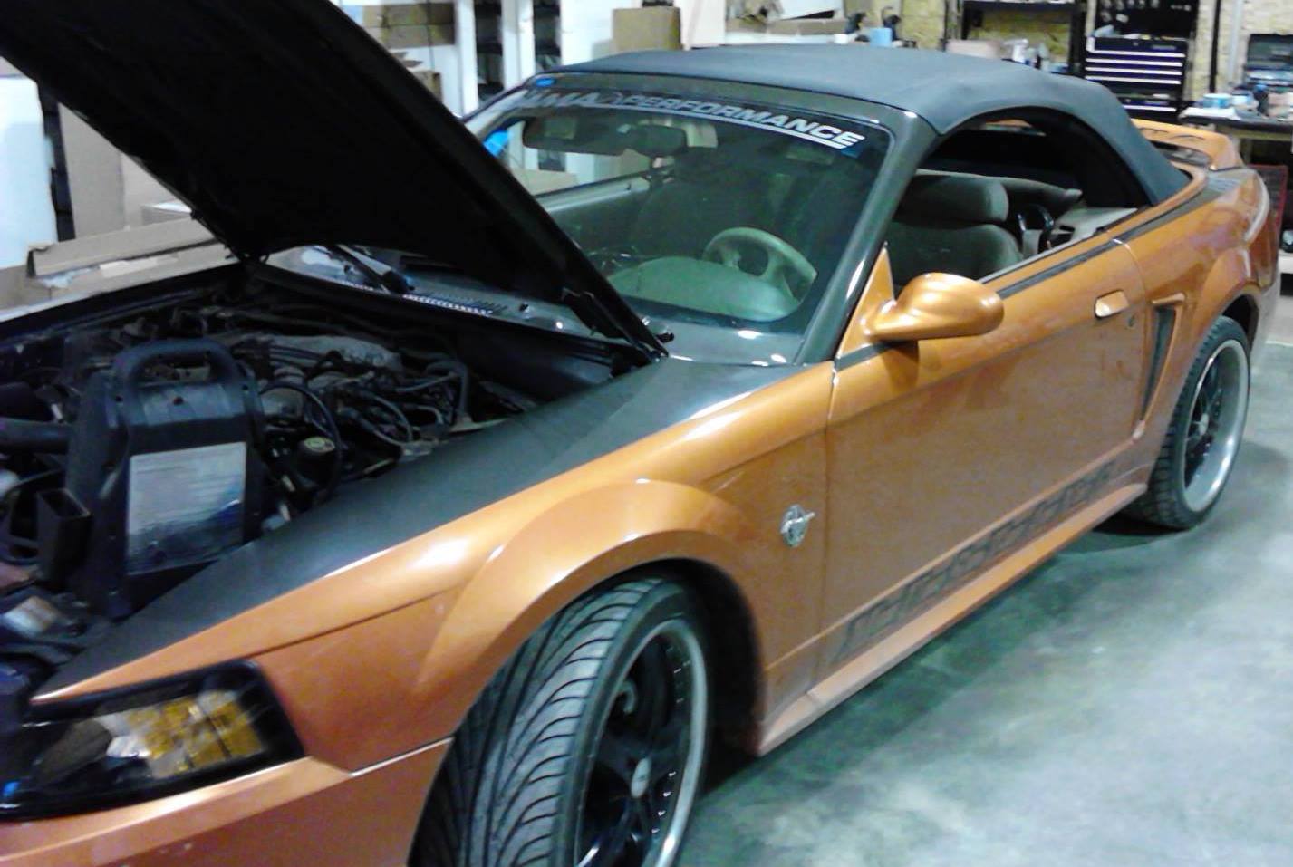 An orange mustang with the hood up in a garage