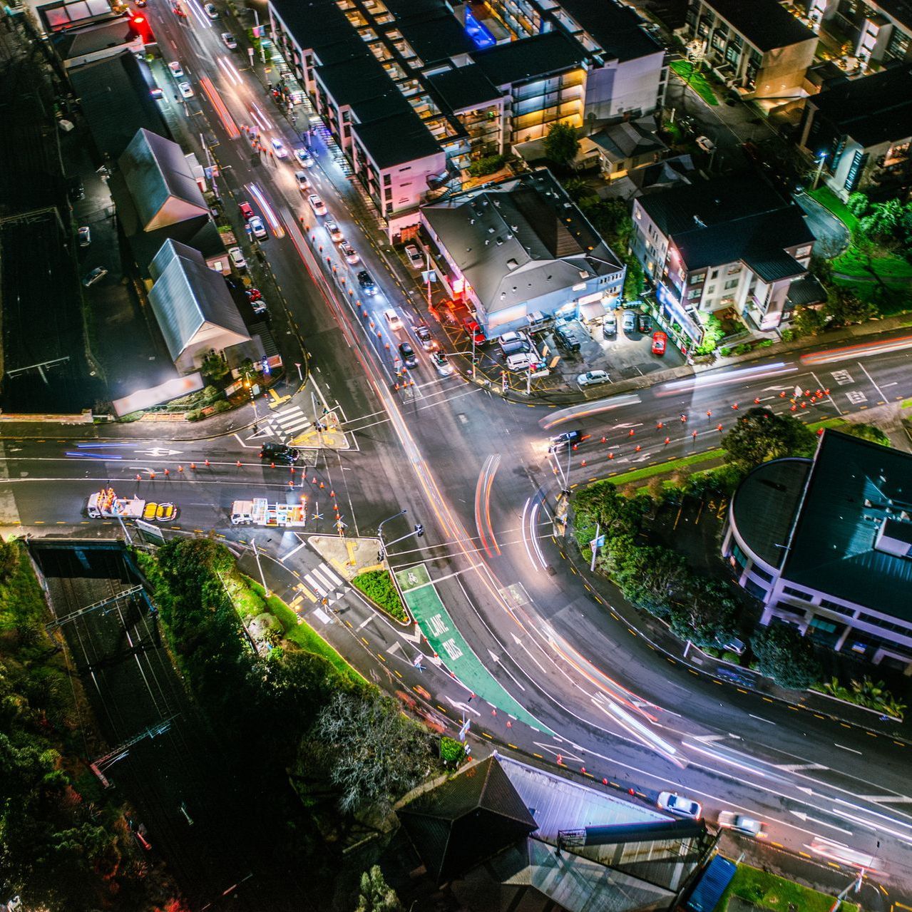 Aerial night view of a busy city intersection with light trails from traffic and surrounding buildings.