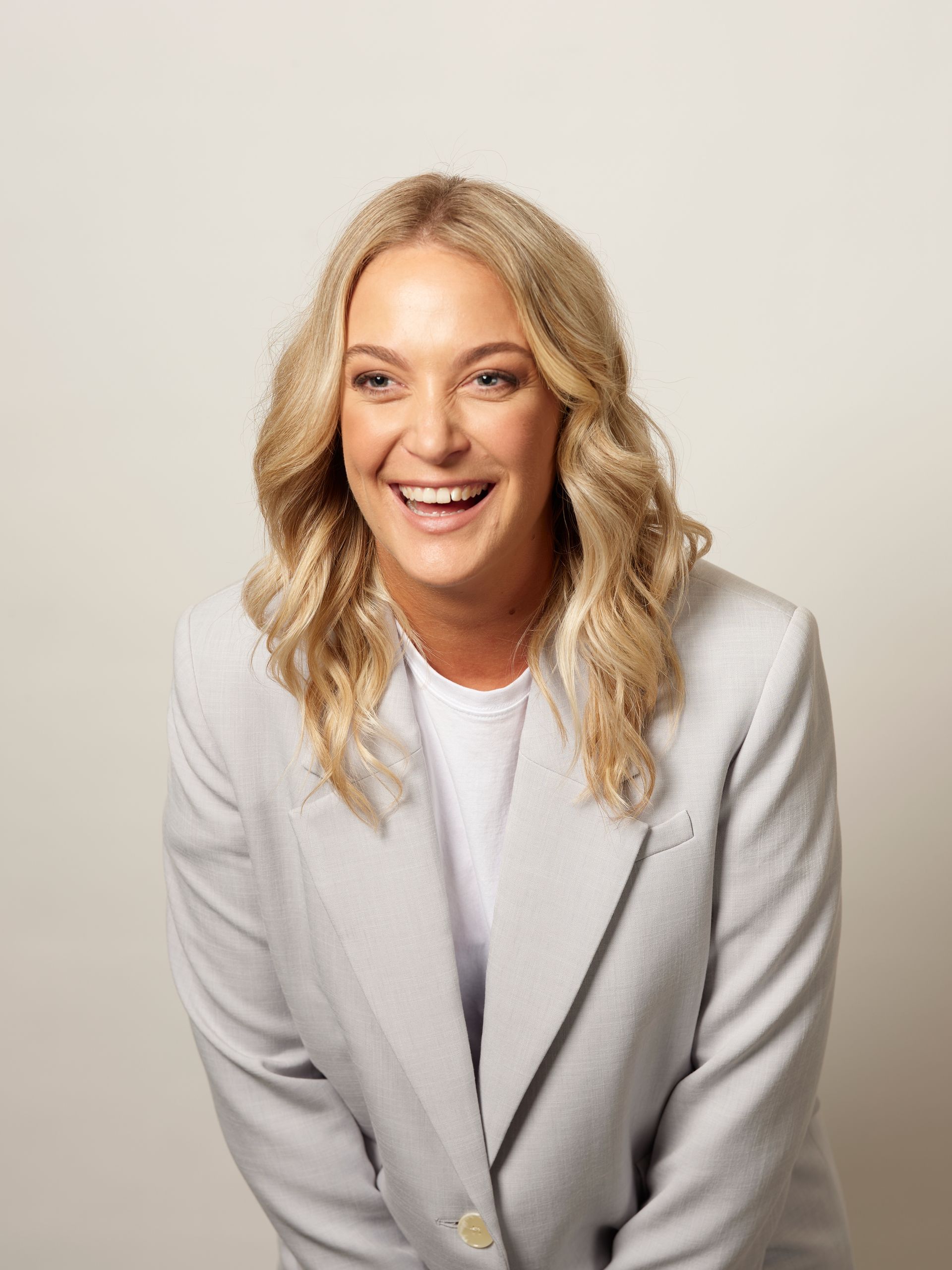 Smiling person in a light gray blazer against a plain background.