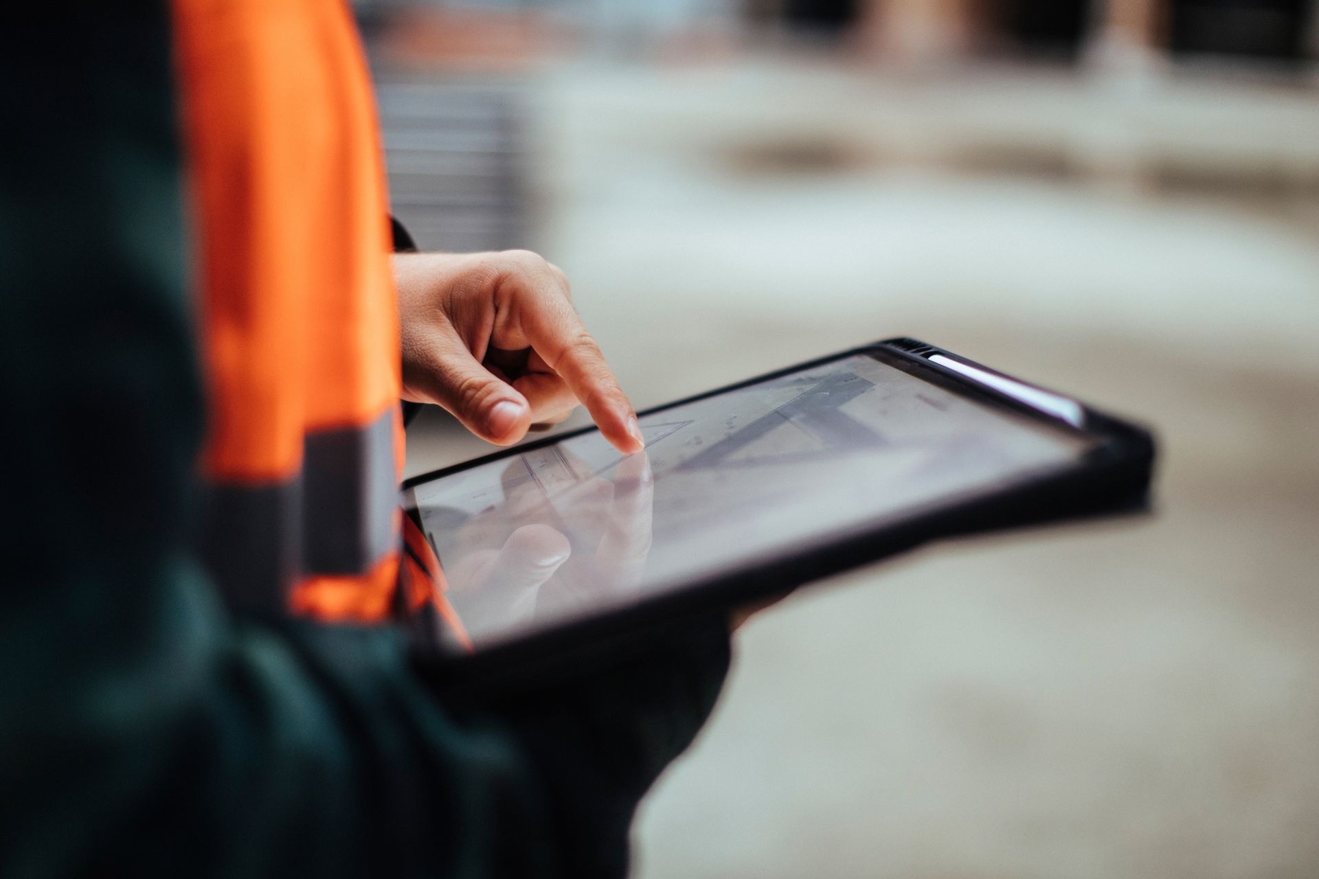 Person in orange vest using a tablet outdoors