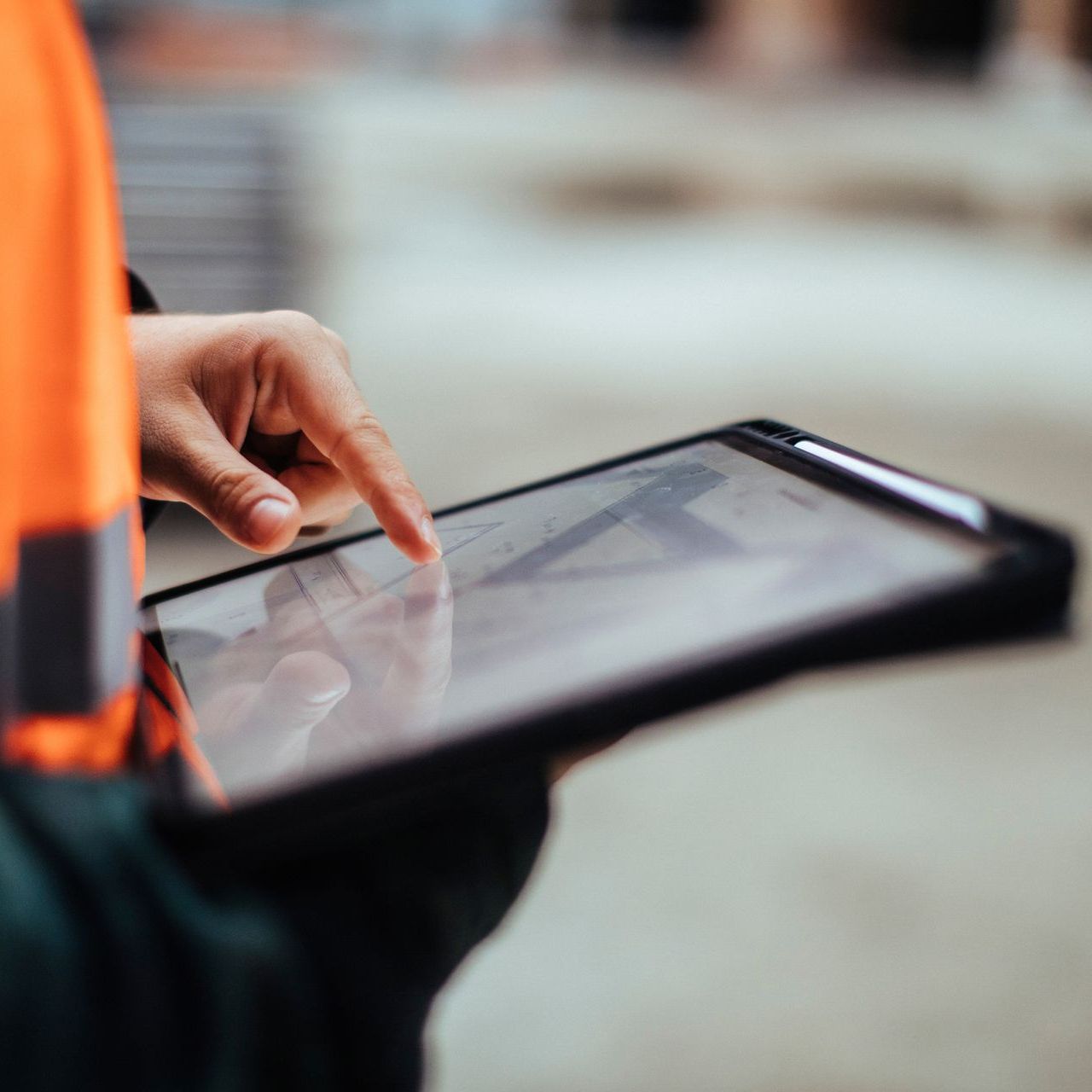 Person using a tablet in a reflective case, wearing an orange jacket, outdoors.