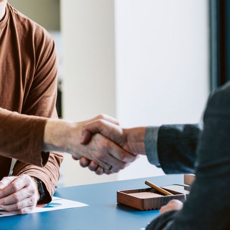 Two people shaking hands across a desk with a pen and notepad.