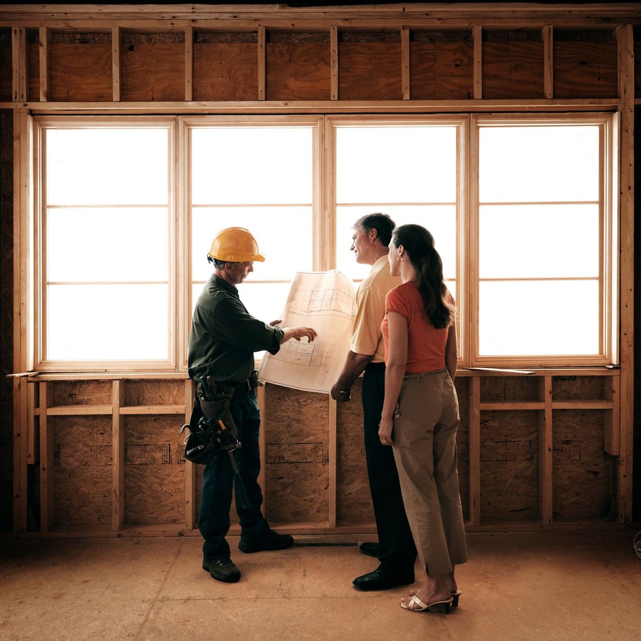 Three people in a construction site review framing plans.