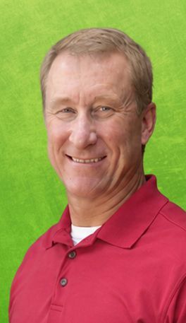 Man in red polo shirt smiles, posing in front of brick wall.