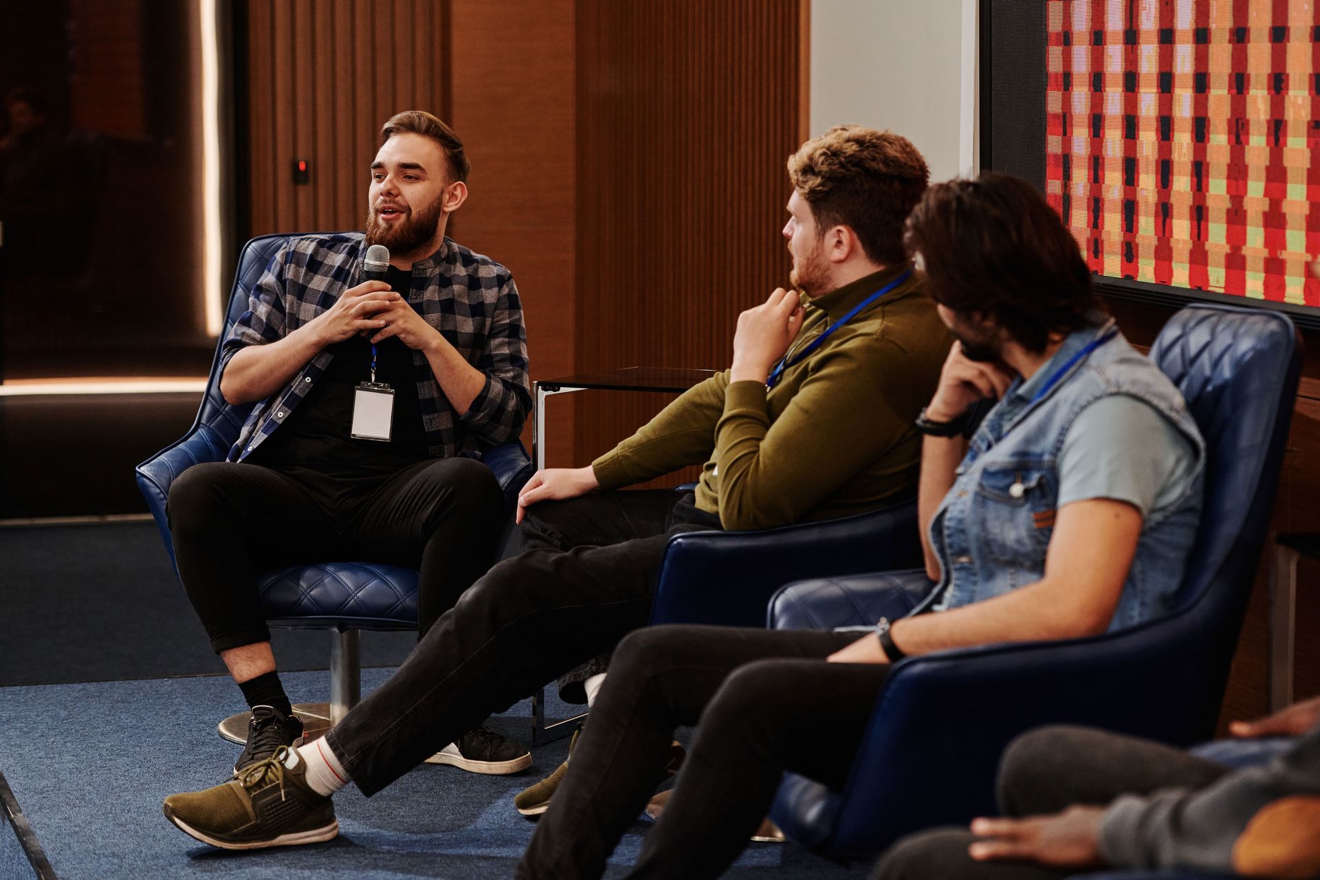 Three people seated on a conference panel, with one speaker holding a microphone while the others li