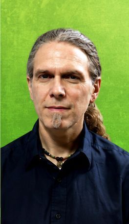 Man with long hair and goatee, wearing a dark blue shirt, against a green background.