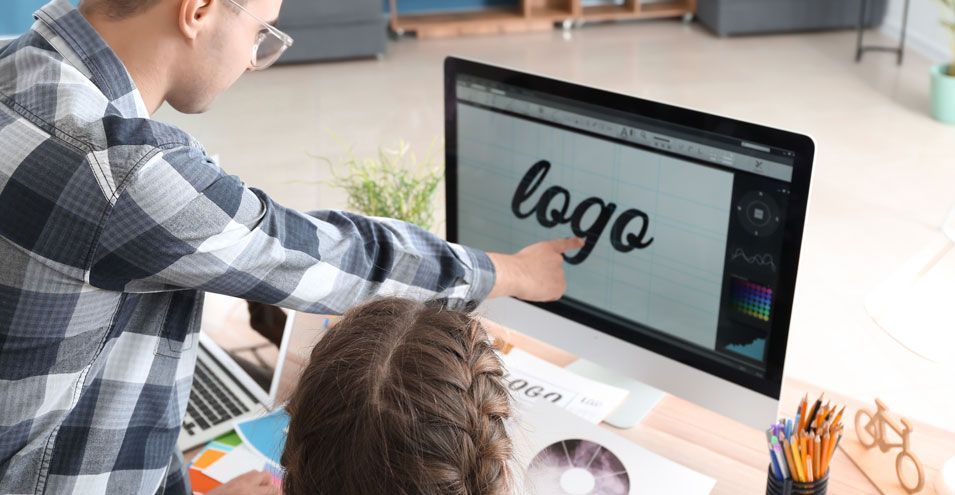 Two people designing a logo on a computer. One points at the word 