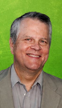 Man in light jacket smiles, green backdrop.