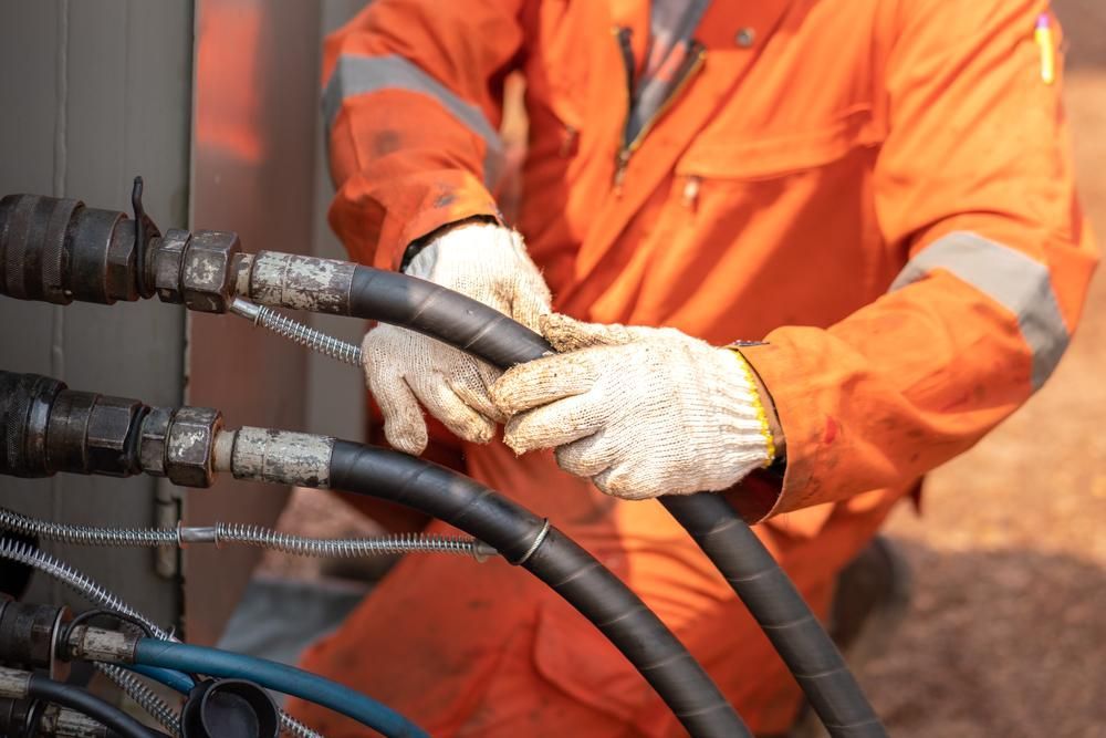 A Man in An Orange Jumpsuit Is Holding a Hose in His Hands — Grafton Hydraulics in South Grafton, NSW