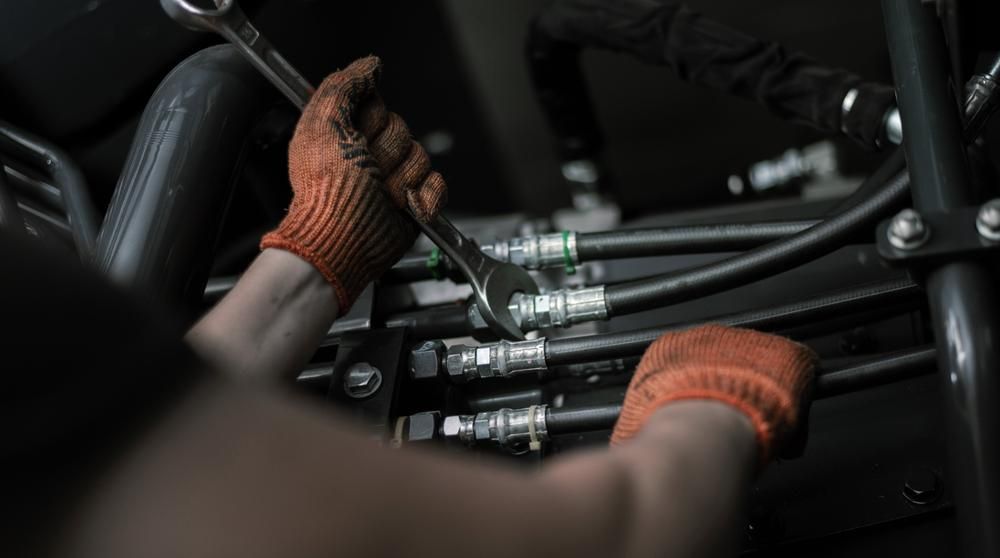 A Man Wearing Orange Gloves is Working on a Machine With a Wrench — Grafton Hydraulics in South Grafton, NSW
