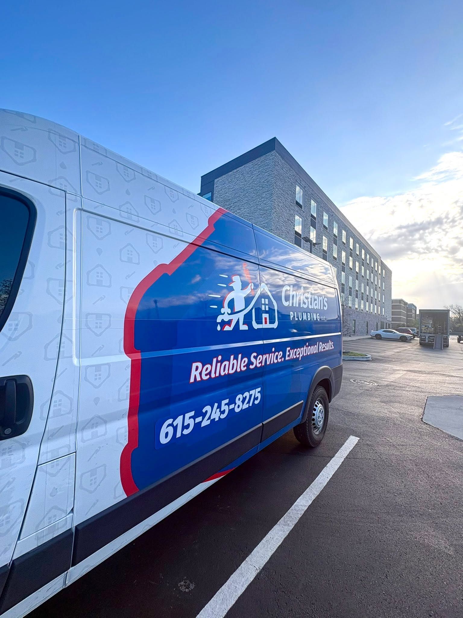 Blue-and-white van with red stripe parked on a street beside a gray building.