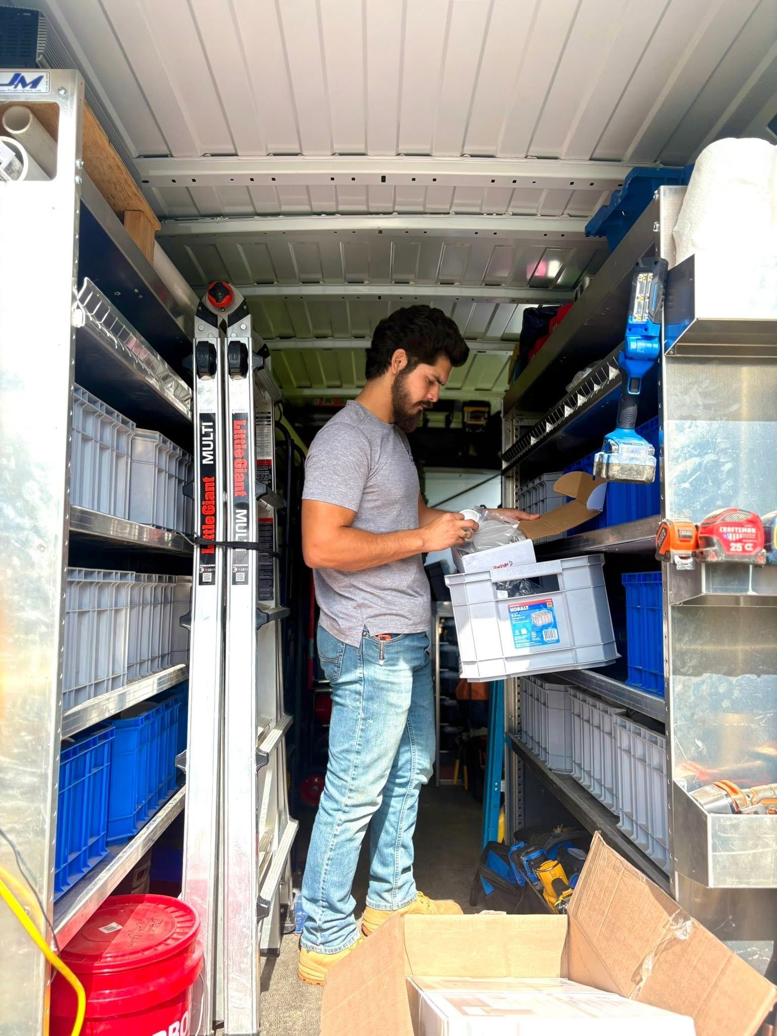 Person stocking shelves in a narrow storage aisle with boxes and supplies