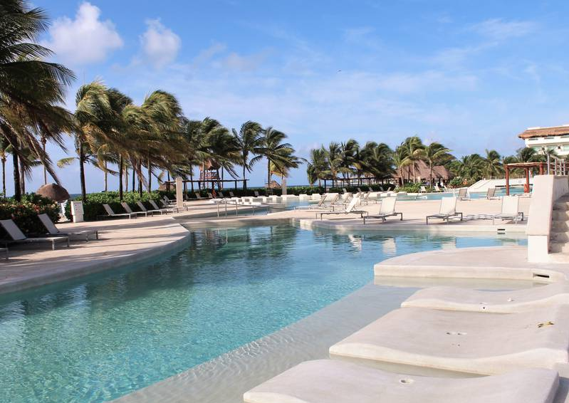 Una gran piscina rodeada de sillas y palmeras