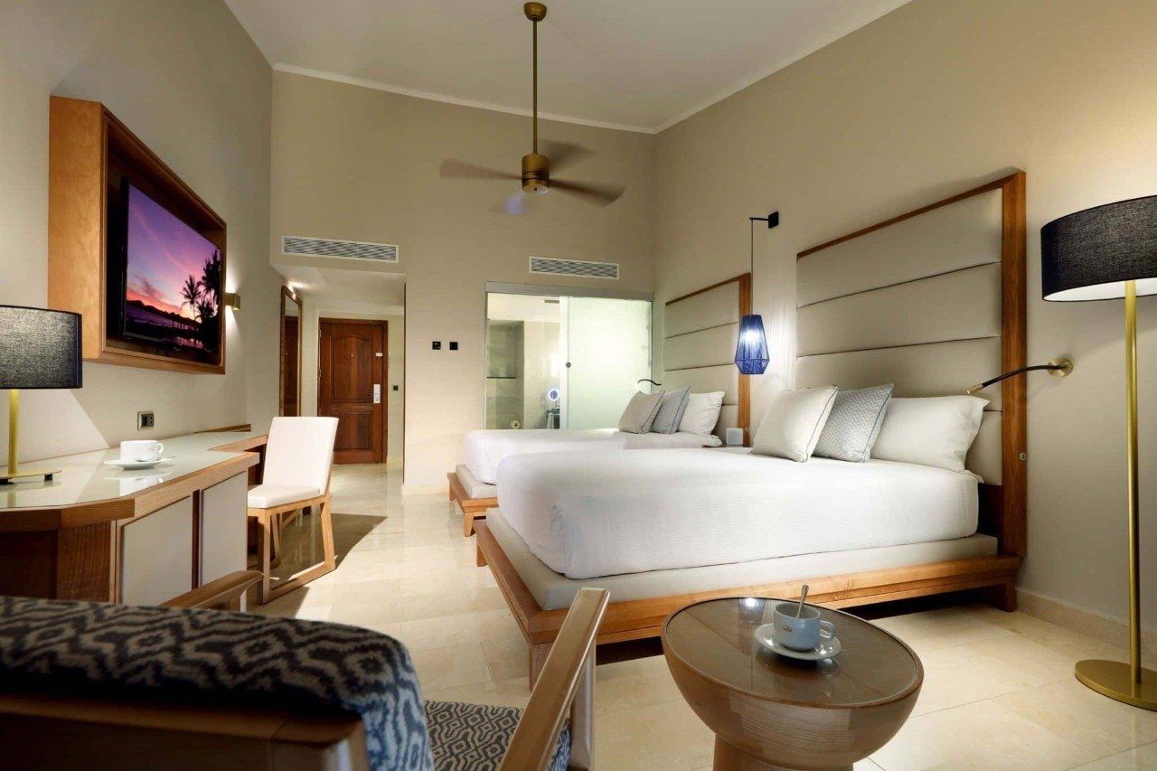 Una habitación de hotel con dos camas, un escritorio, un televisor y un ventilador de techo.