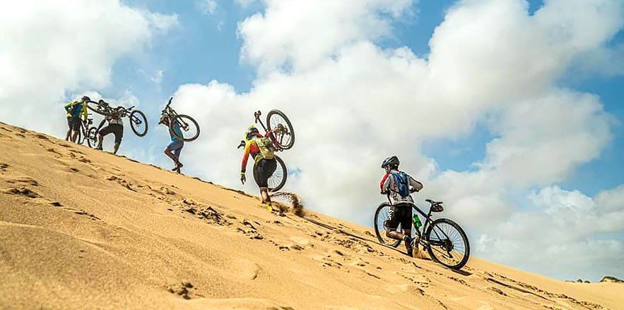 Un grupo de personas sube en bicicleta por una duna de arena.