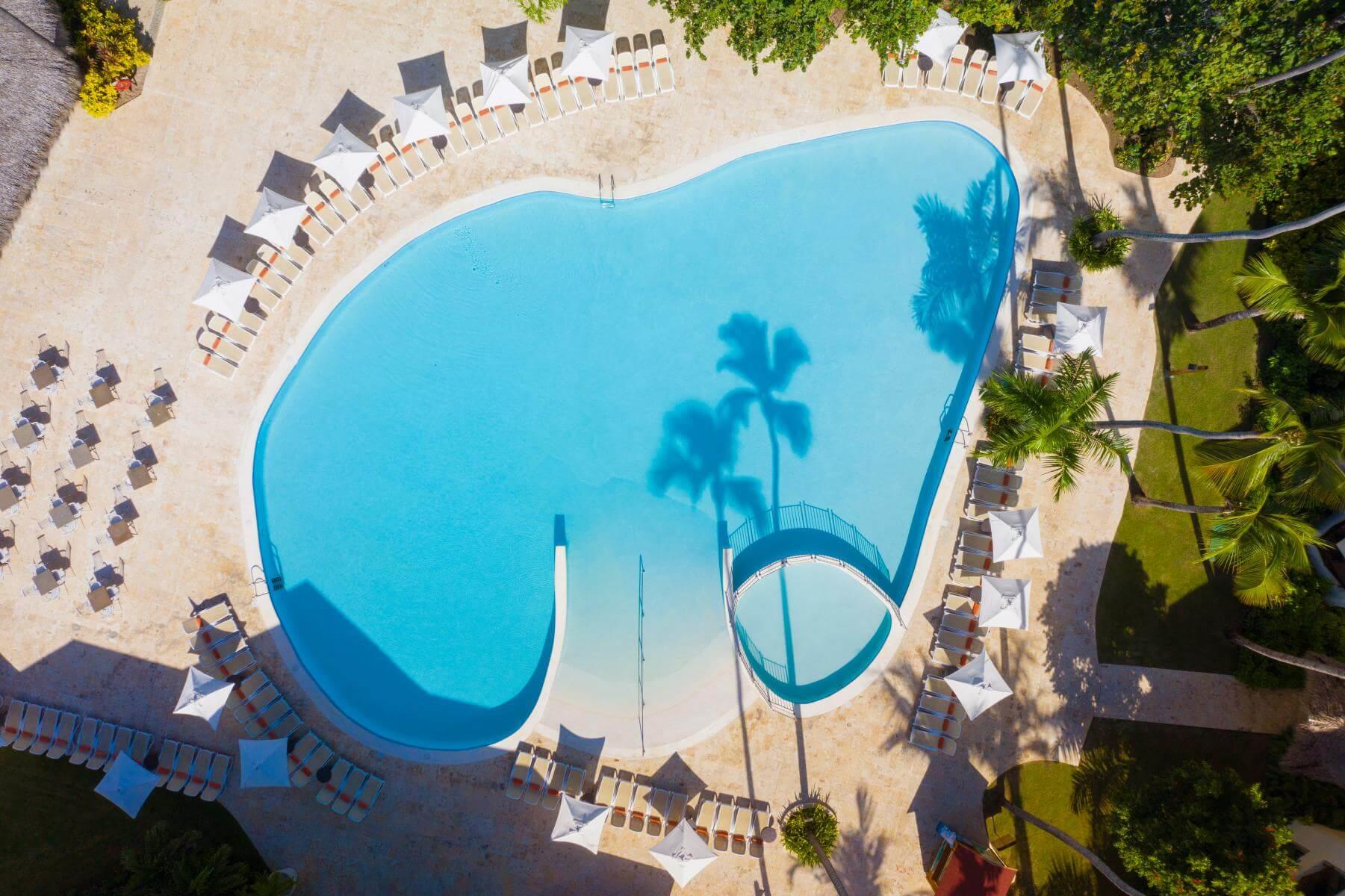 Una vista aérea de una gran piscina rodeada de sillas y palmeras.