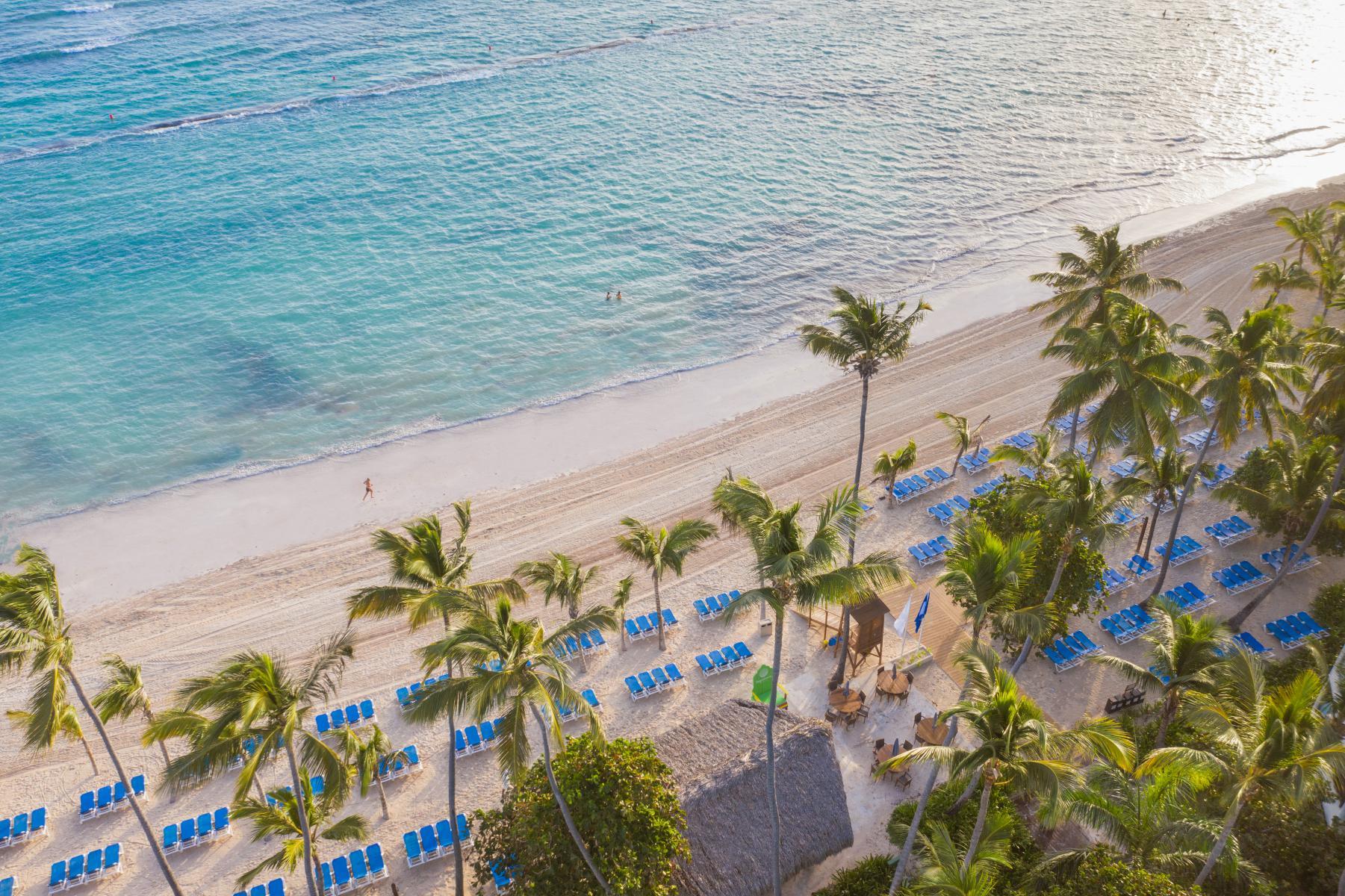 Una vista aérea de una playa tropical con palmeras y sombrillas azules.