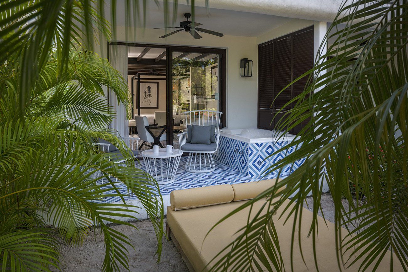 Un patio con sofá , sillas , mesas y ventilador de techo rodeado de palmeras.