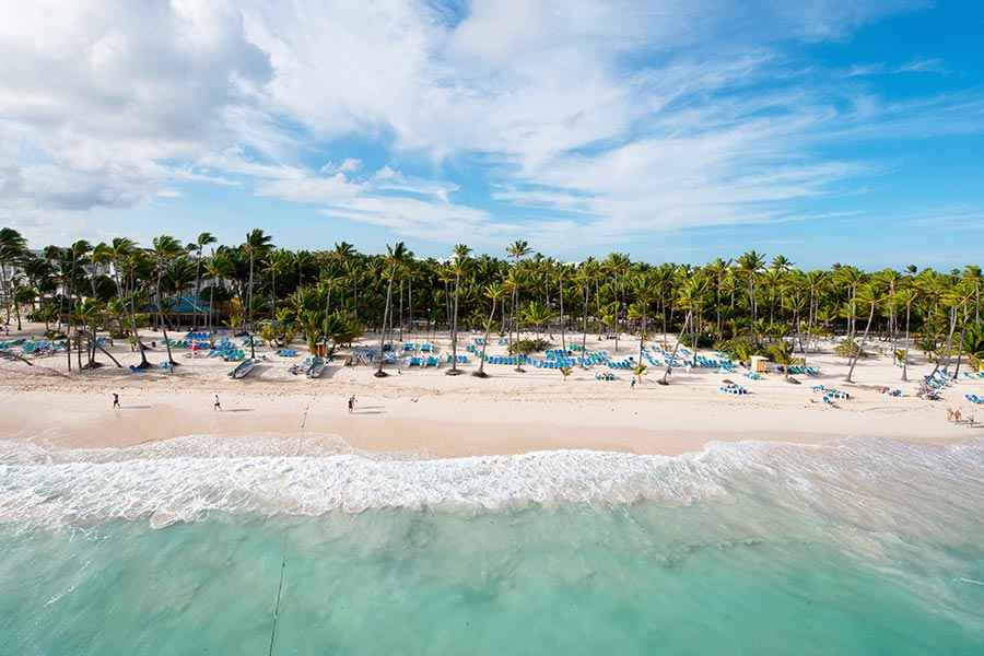 Una vista aérea de una playa tropical con palmeras y sombrillas.