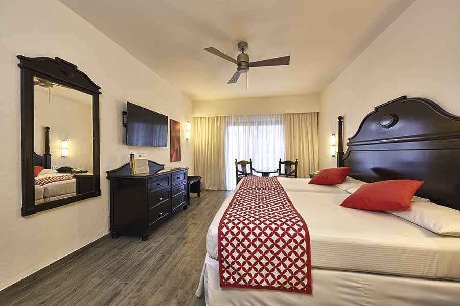 Una habitación de hotel con dos camas, una cómoda, un espejo y un ventilador de techo.
