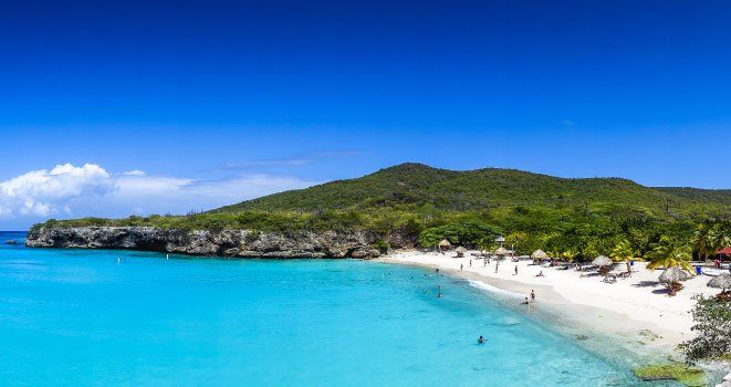 Una playa con una montaña al fondo y gente nadando en el agua.