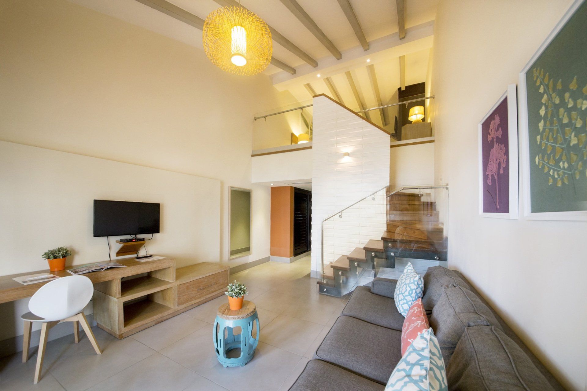 Una sala de estar con sofá, escritorio, televisión y escaleras.