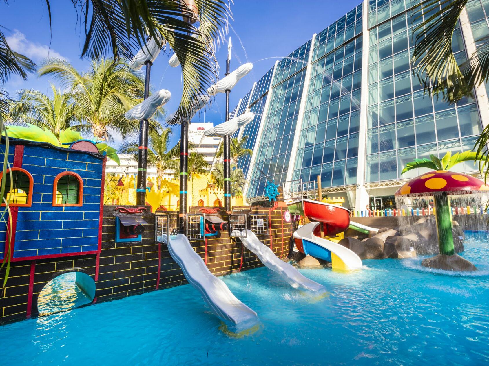 Un parque acuático con tobogán y un barco pirata delante de un edificio.