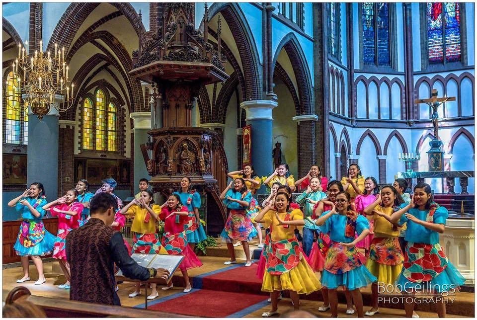 A group of people are dancing in a church while a man holds a sheet of music.