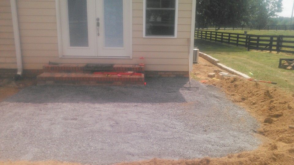 A patio is being built in front of a house with a fence in the background.