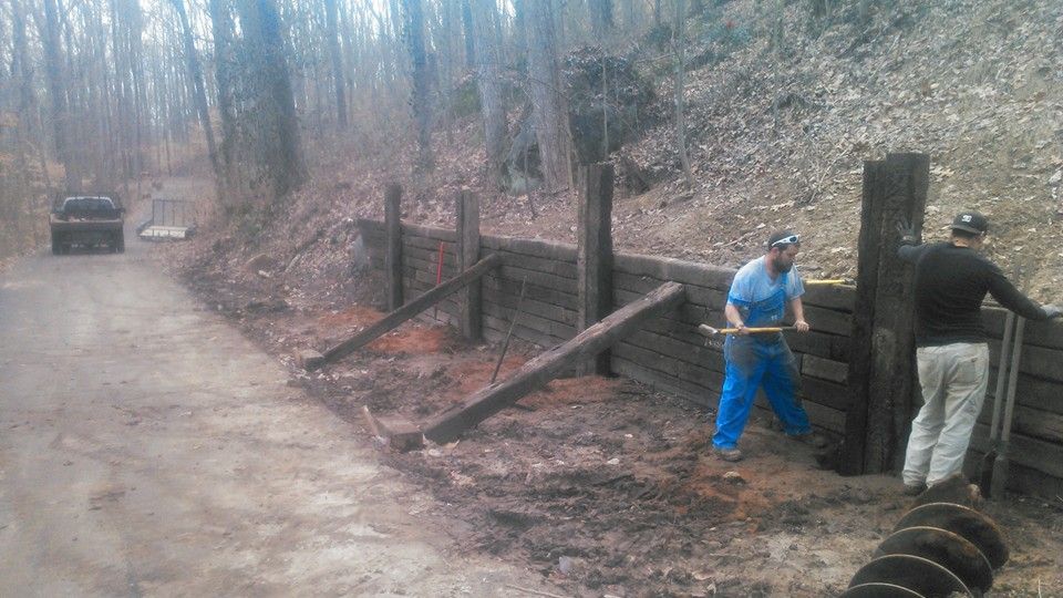 Two men are working on a wooden fence in the woods.