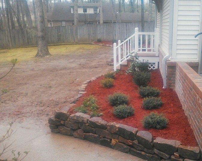 A house with a stone wall and red mulch in front of it