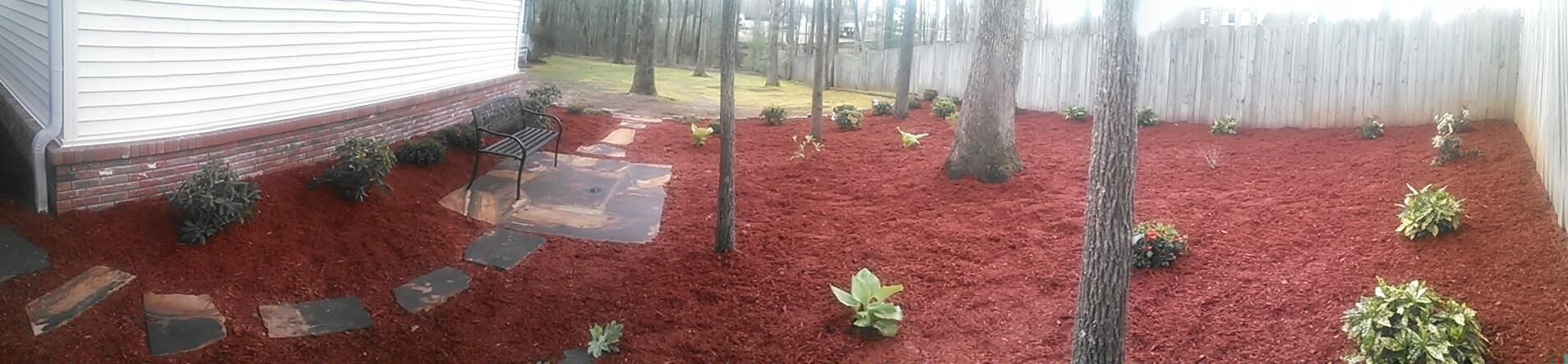 A backyard filled with red mulch and trees.