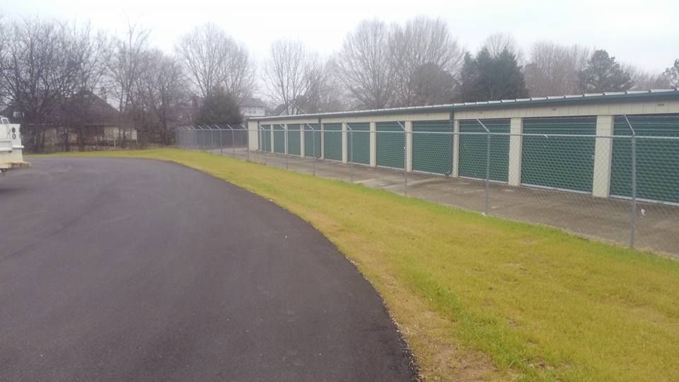 A driveway leading to a row of storage units behind a fence.