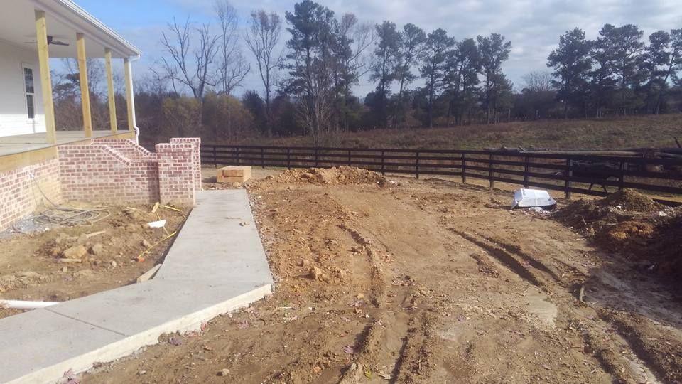 A dirt path leading to a house with a fence in the background.